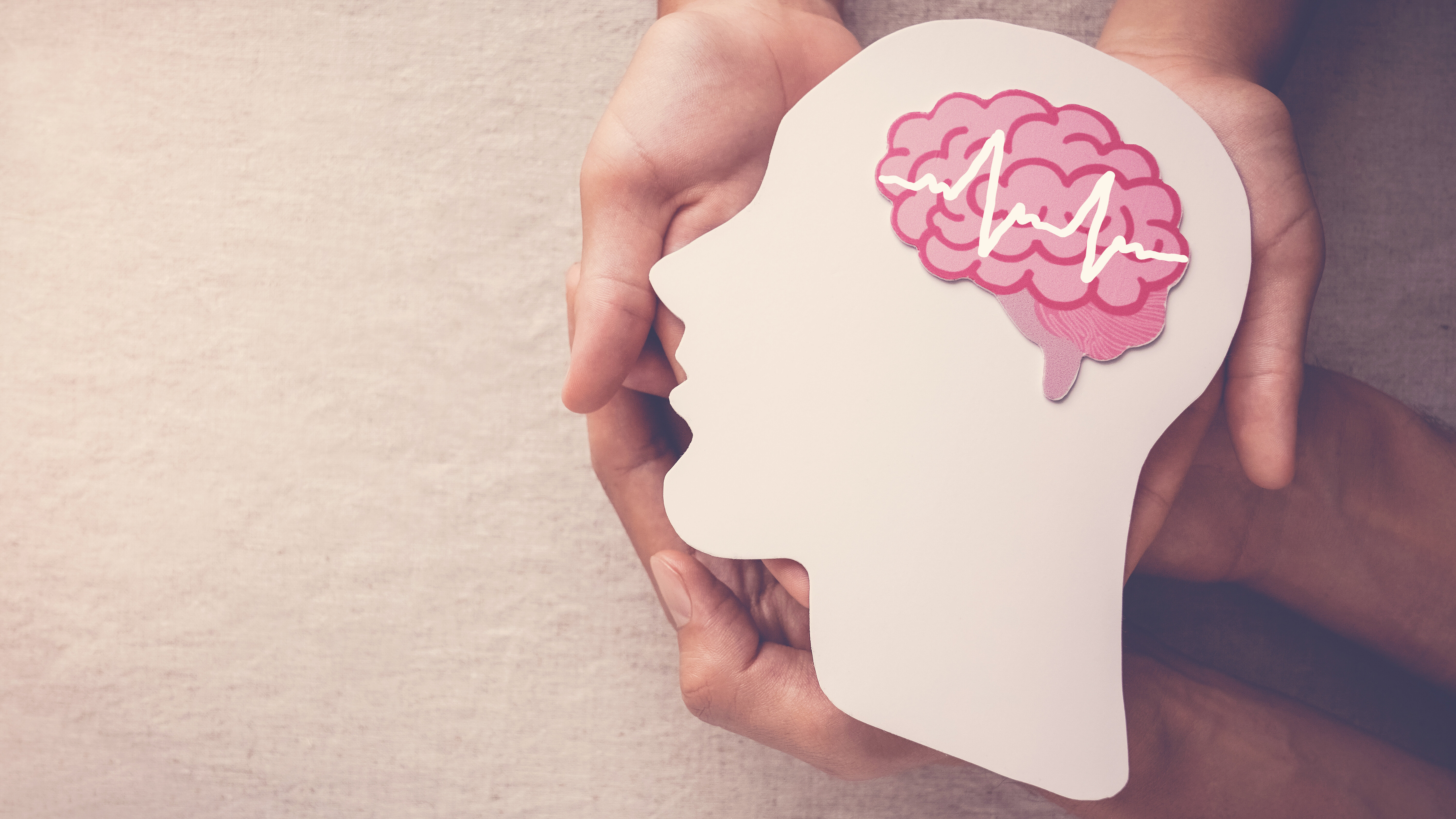 Hände halten die Silhouette eines Kopfes mit einem hervorgehobenen Gehirn als Symbol für mentale Gesundheit und neurologische Versorgung.