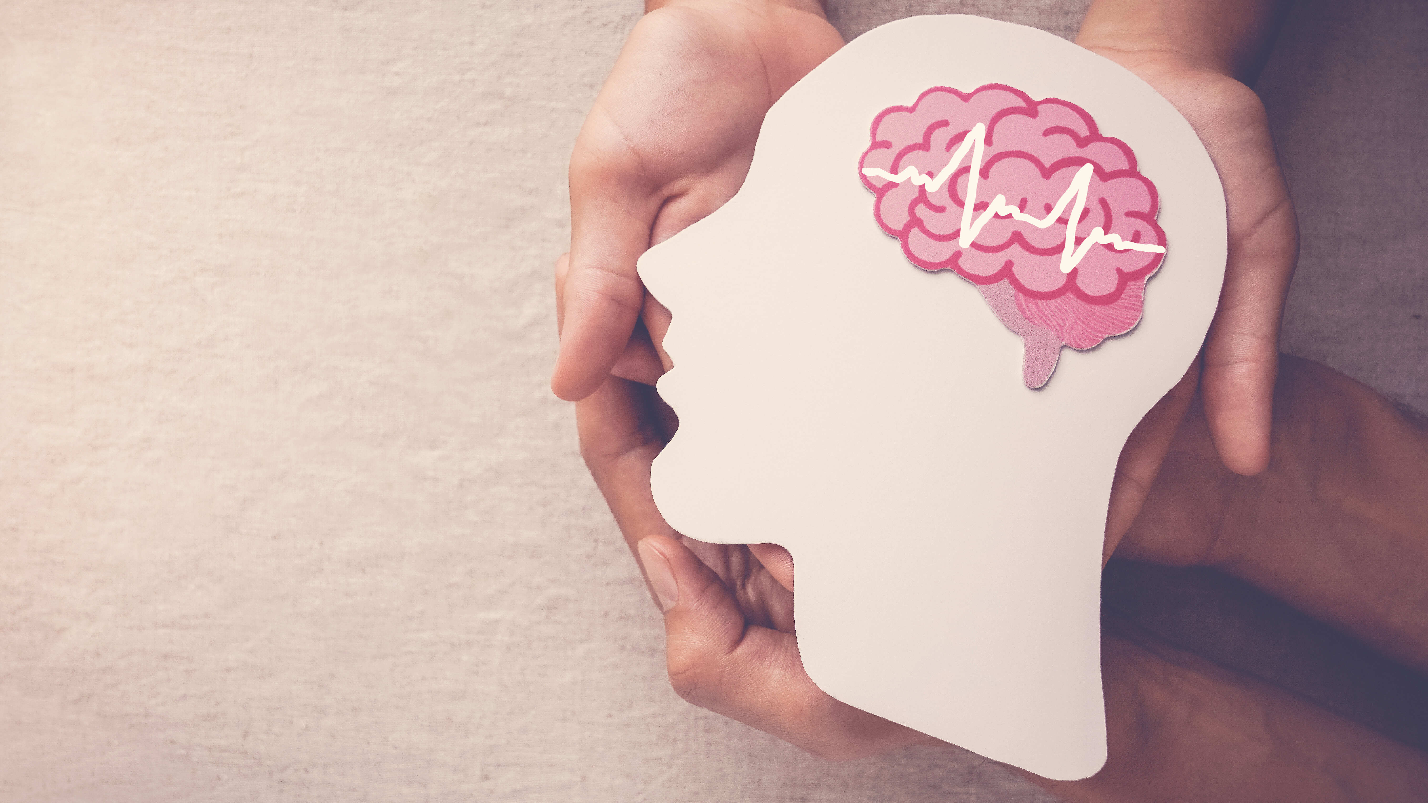 Hands hold the silhouette of a head with a highlighted brain, symbolizing mental health and neurological care.