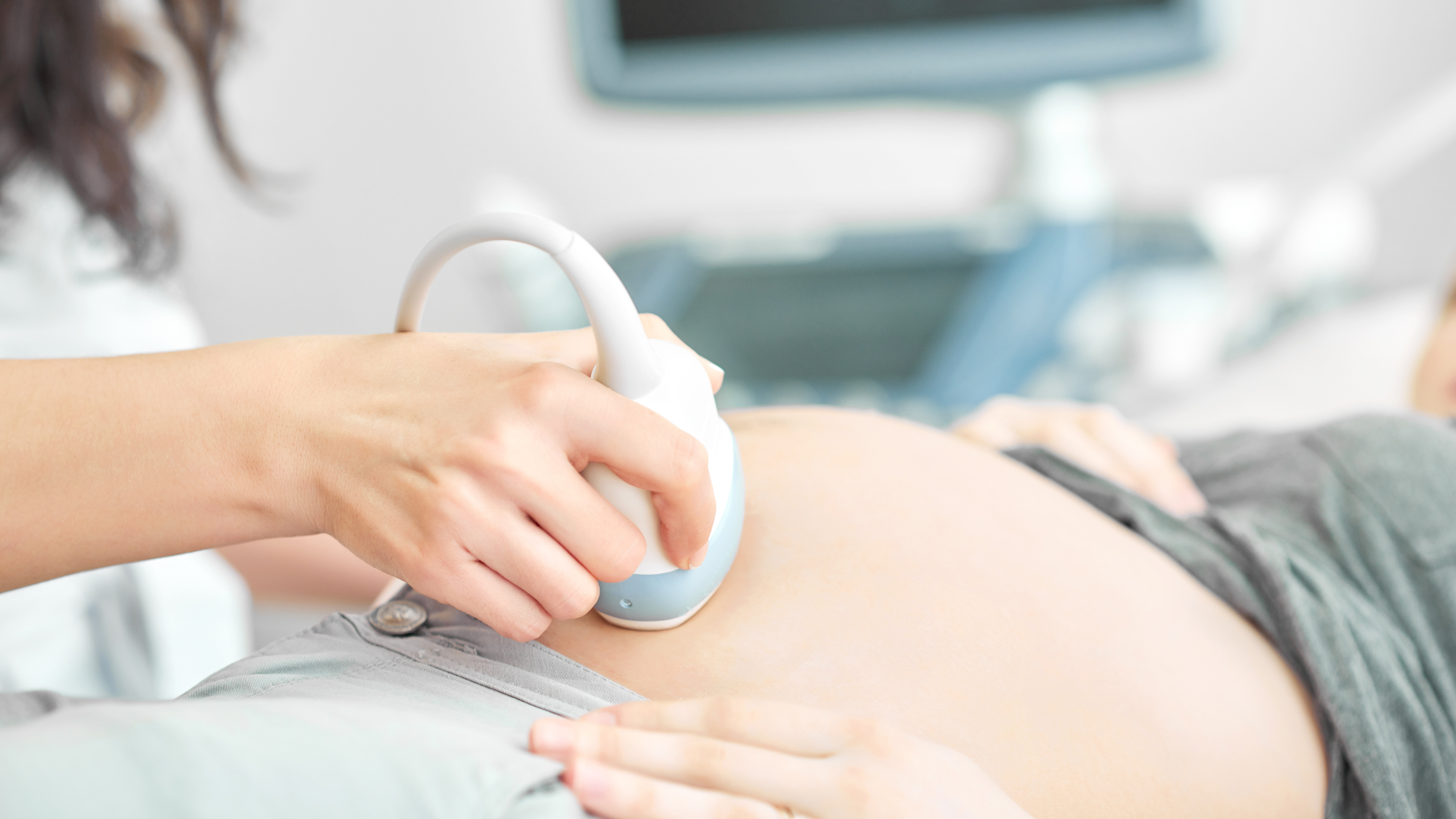 Ultraschalluntersuchung während einer Schwangerschaft mit Ultraschallsonde auf dem Bauch einer Patientin.