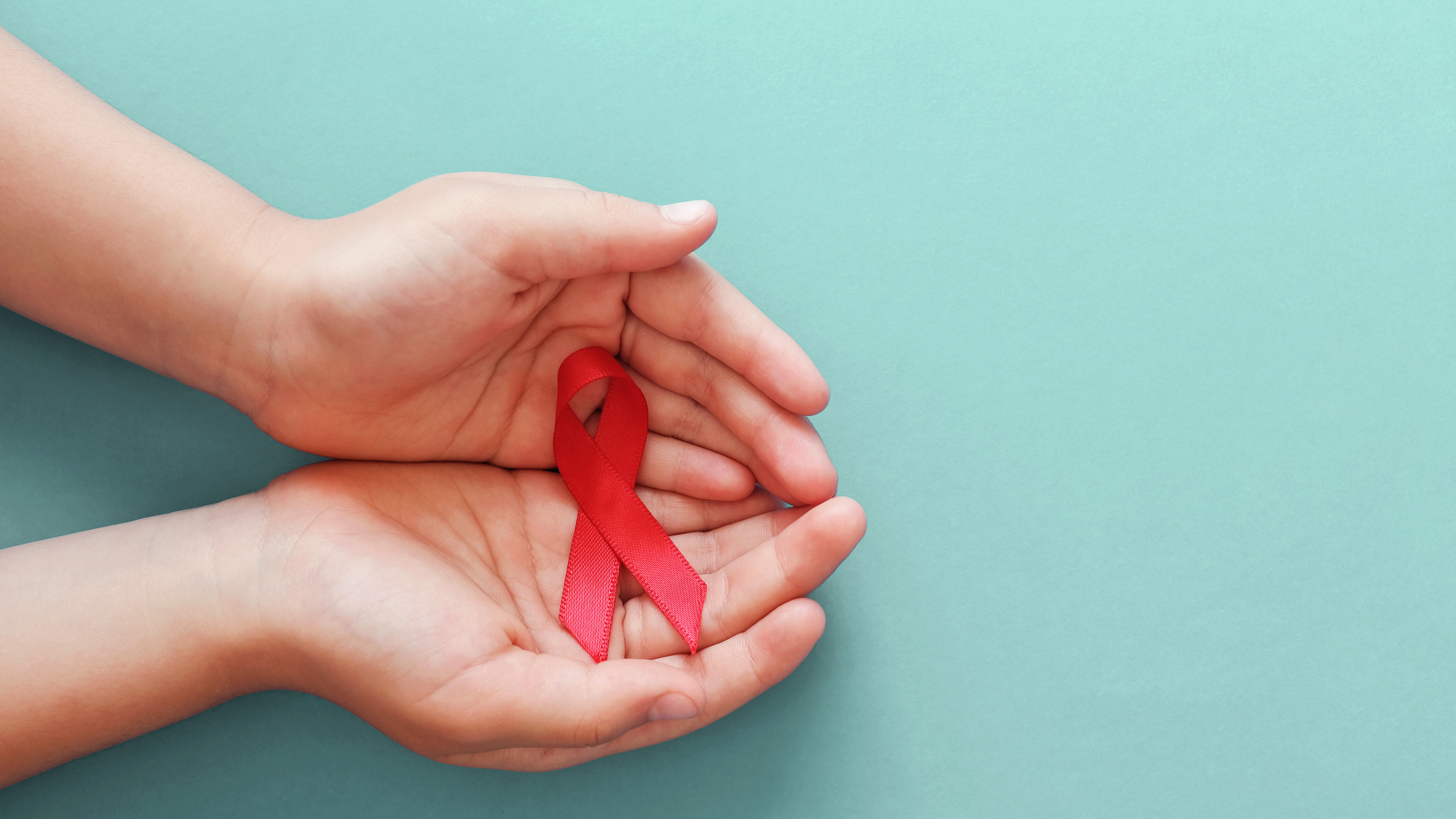 Two hands holding a red ribbon as a symbol of awareness, support, and solidarity in health-related contexts.