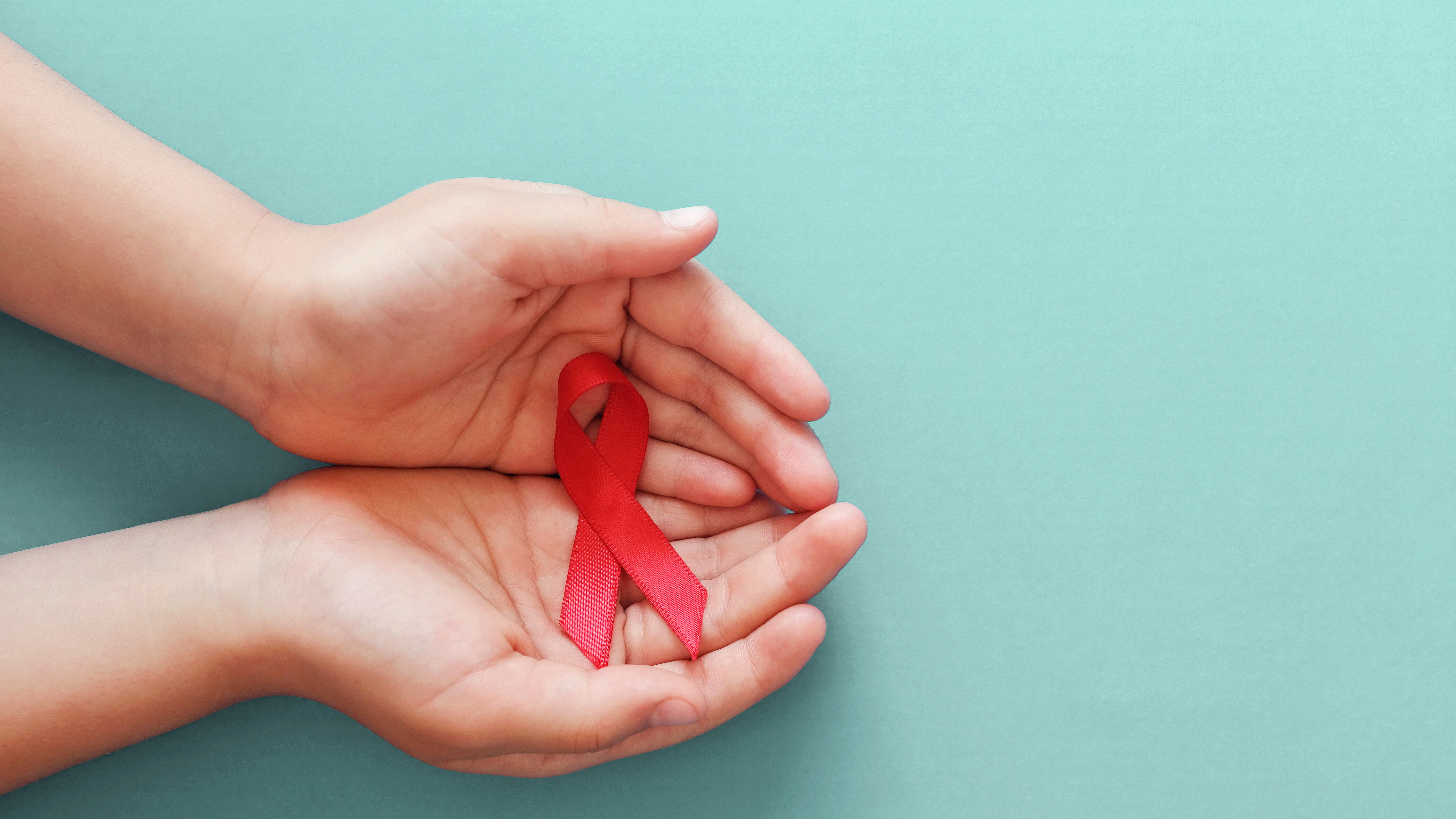 Zwei Hände halten eine rote Schleife als Symbol für Aufklärung, Solidarität und Unterstützung bei gesundheitlichen Themen.