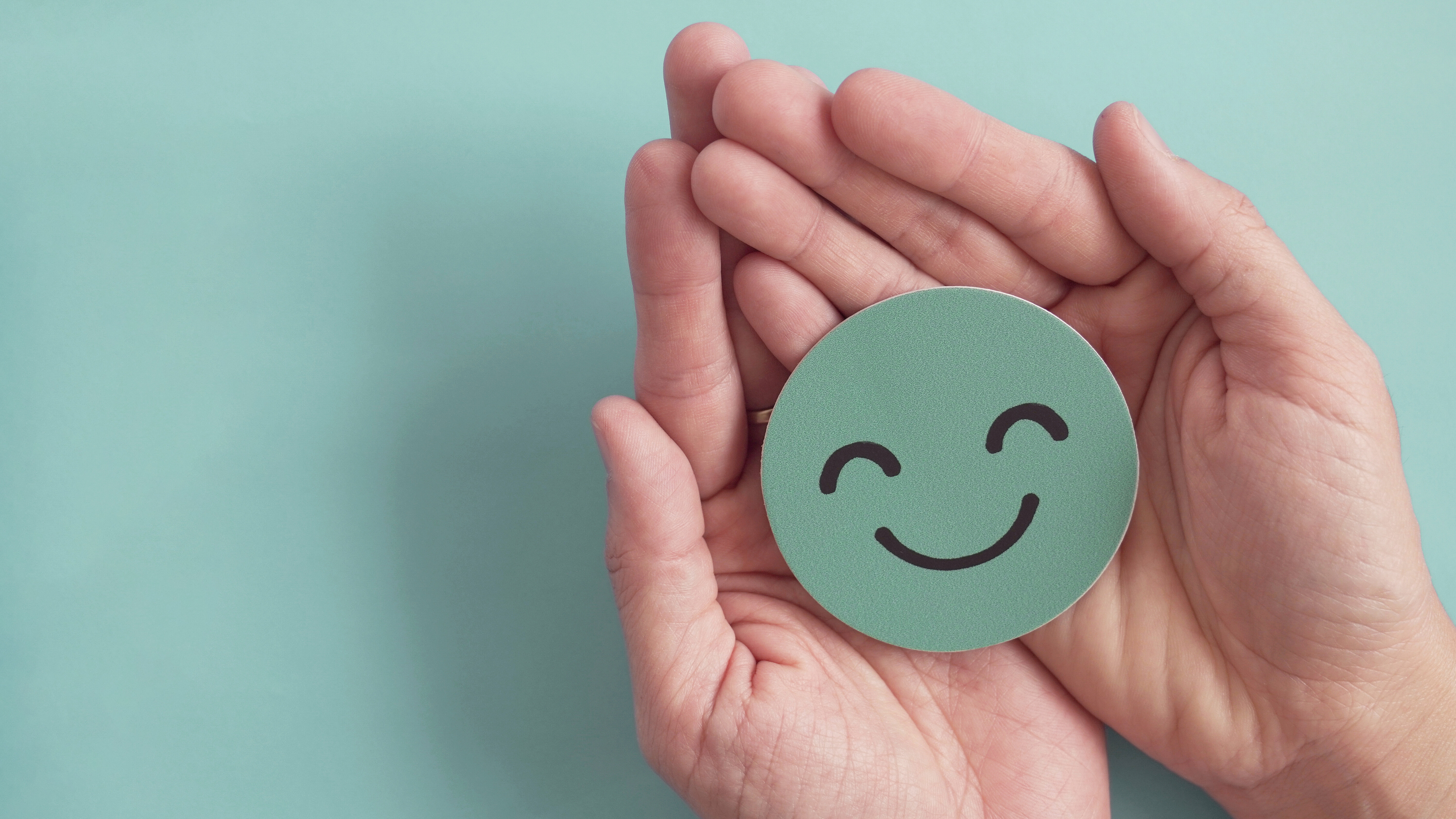 Hände halten ein Smiley-Symbol als Zeichen für Wohlbefinden, Lebensqualität und positive mentale Gesundheit.