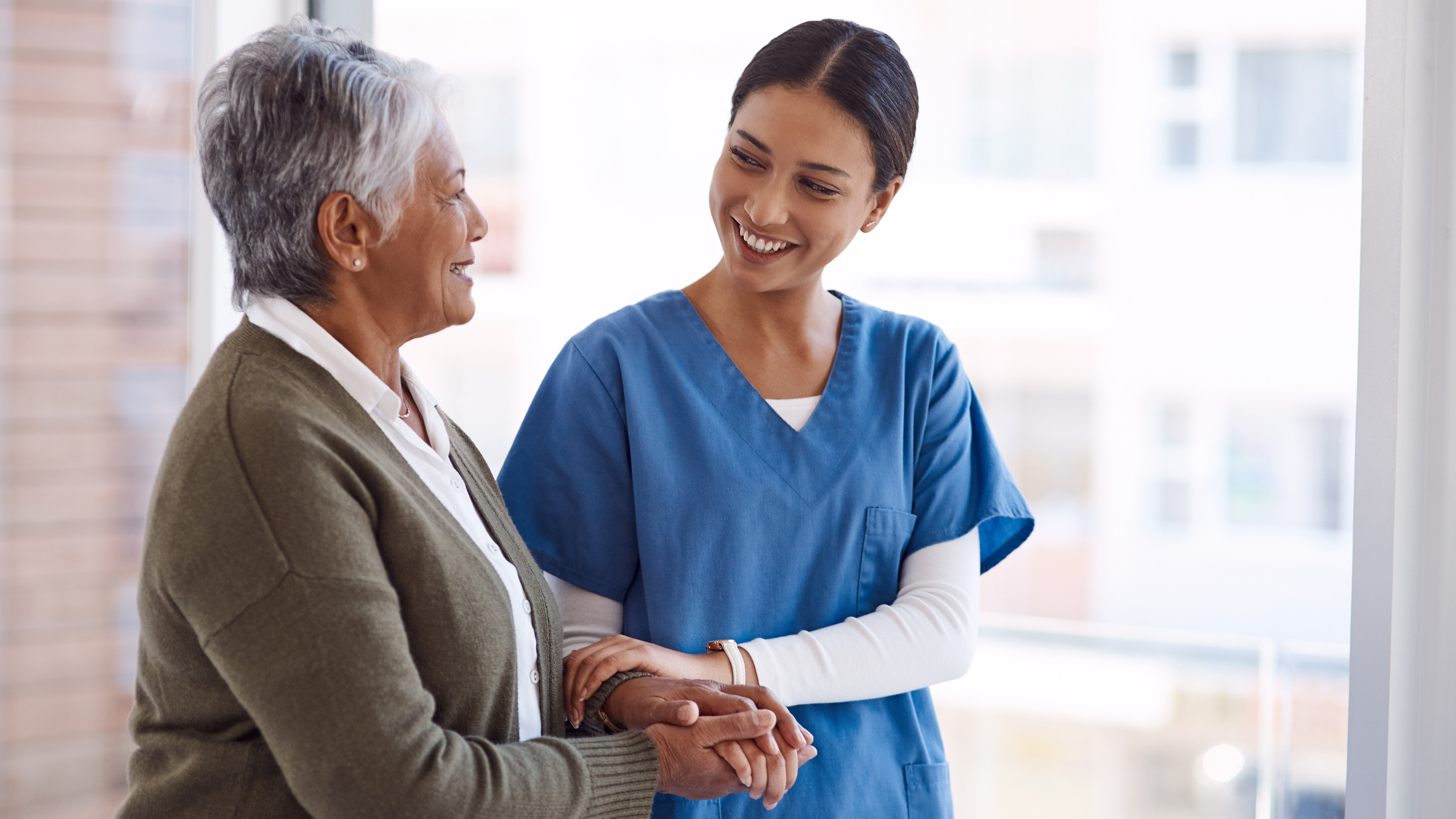 Healthcare worker holding the hand of an older person in a bright healthcare setting.
