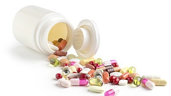 Open medication container with various tablets and capsules scattered on a surface.