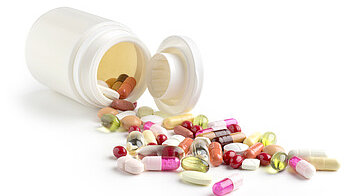 Open medication container with various tablets and capsules scattered on a surface.