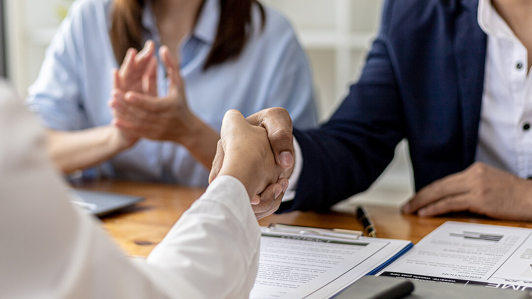 Handshake over documents during a meeting, symbolizing collaboration and agreement.